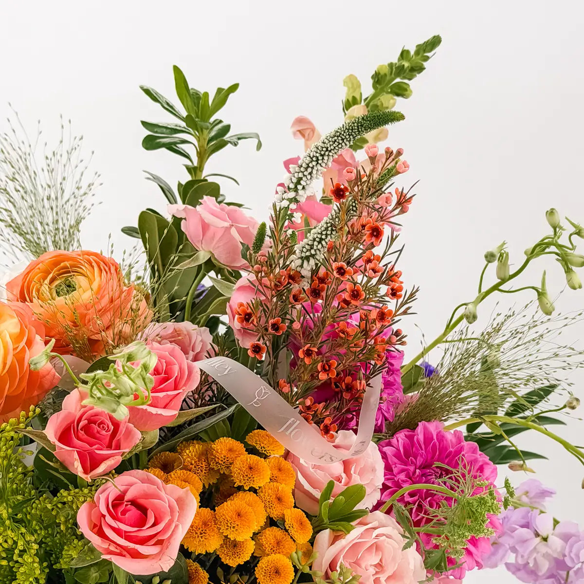 Close-up of Indigo Harvest fall flowers: pink spray roses, orange waxflower, white veronica, golden mums and Flowers Valley ribbon