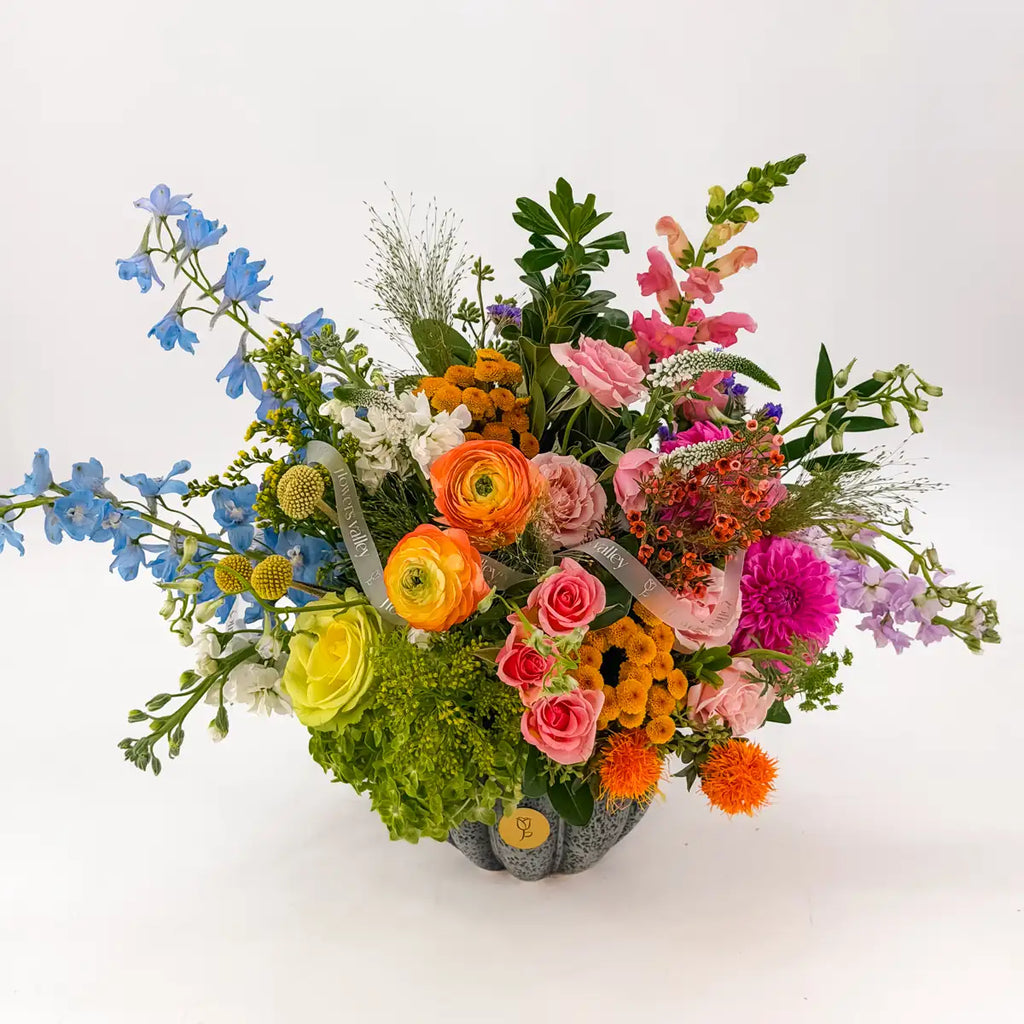 Colorful autumn arrangement Indigo Harvest seen from above: delphinium, ranunculus, fuchsia dahlia, snapdragons and button mums in a pumpkin vase