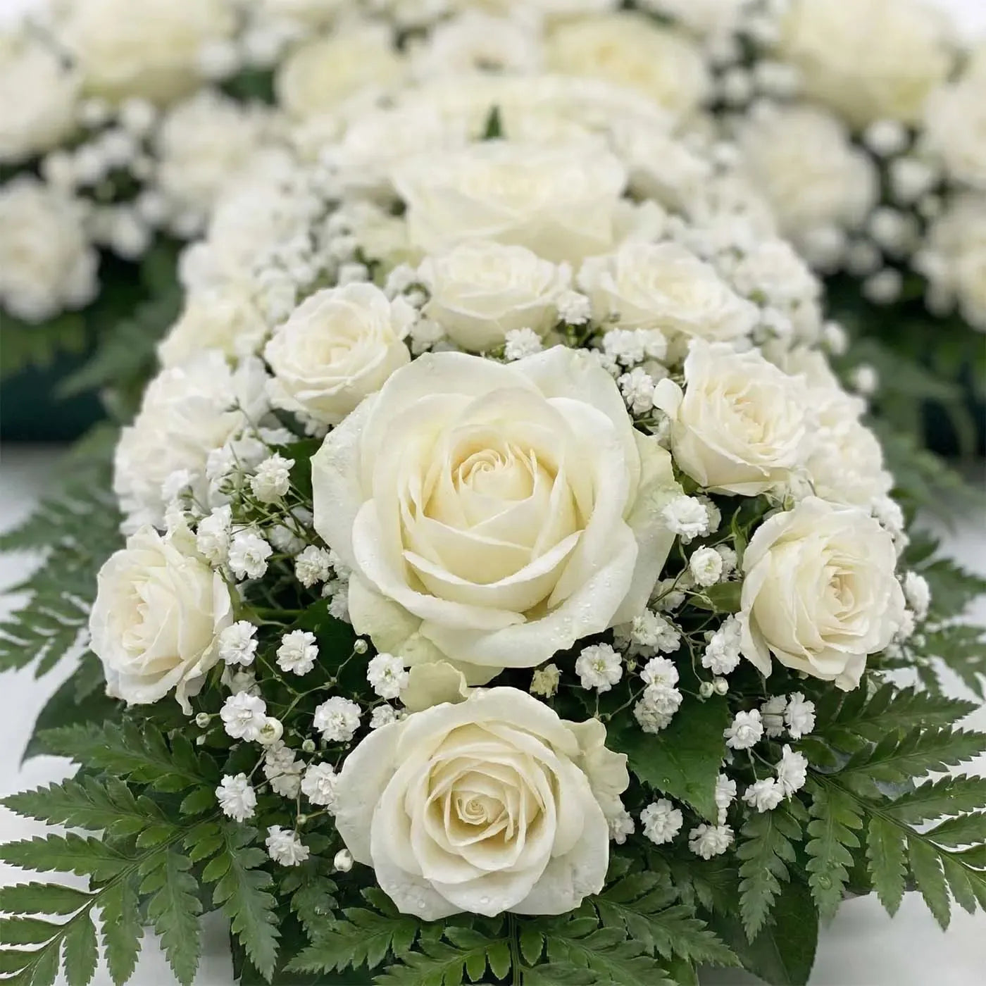 Close-up of Ivory Passage standing floral cross with ivory roses, white carnations, and baby’s breath