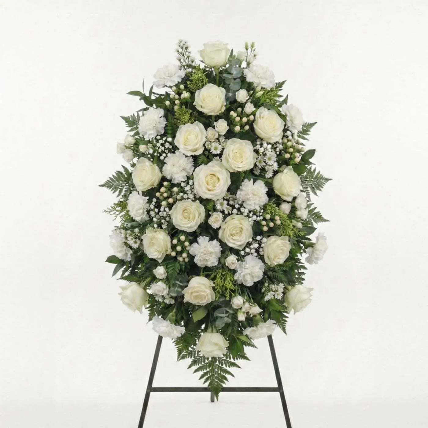 Grand white standing funeral spray with ivory roses, white carnations, baby’s breath, and fern greenery on an easel