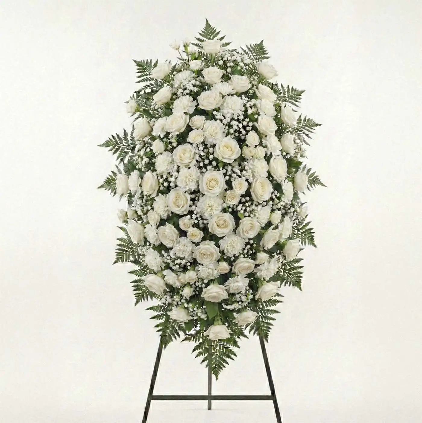 Majestic white standing funeral spray with dense ivory roses, white carnations, baby’s breath, and fern greenery on an easel