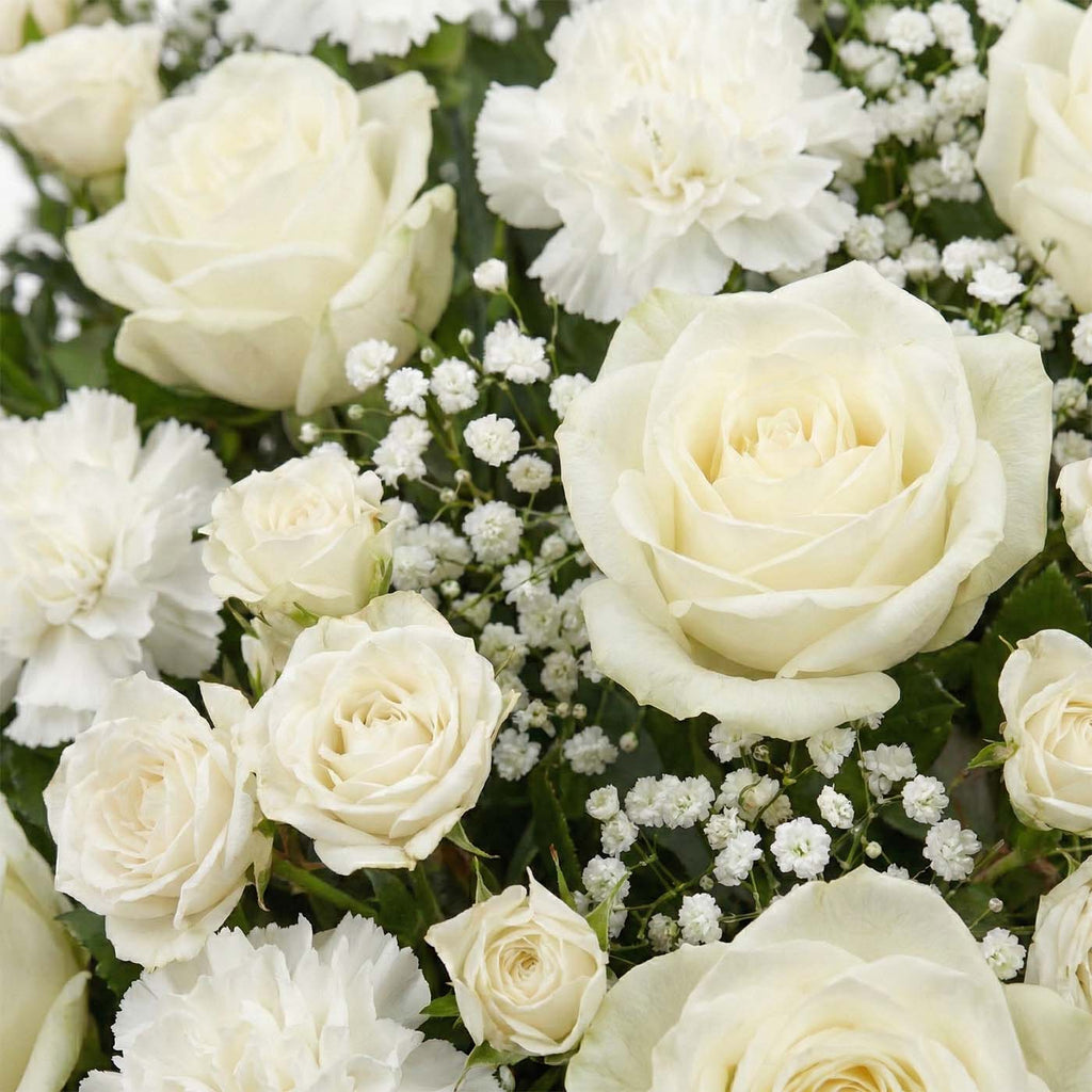 Close-up of Ivory Passage sympathy basket with ivory roses, white carnations, baby’s breath, and greenery