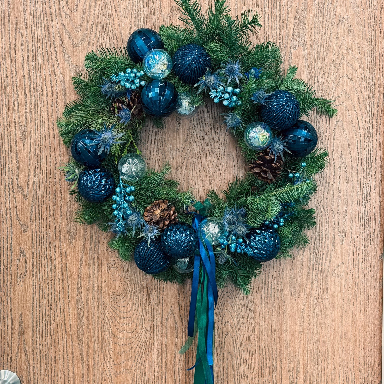 Luxury blue Christmas wreath with fresh evergreens and sapphire ornaments on a wooden door