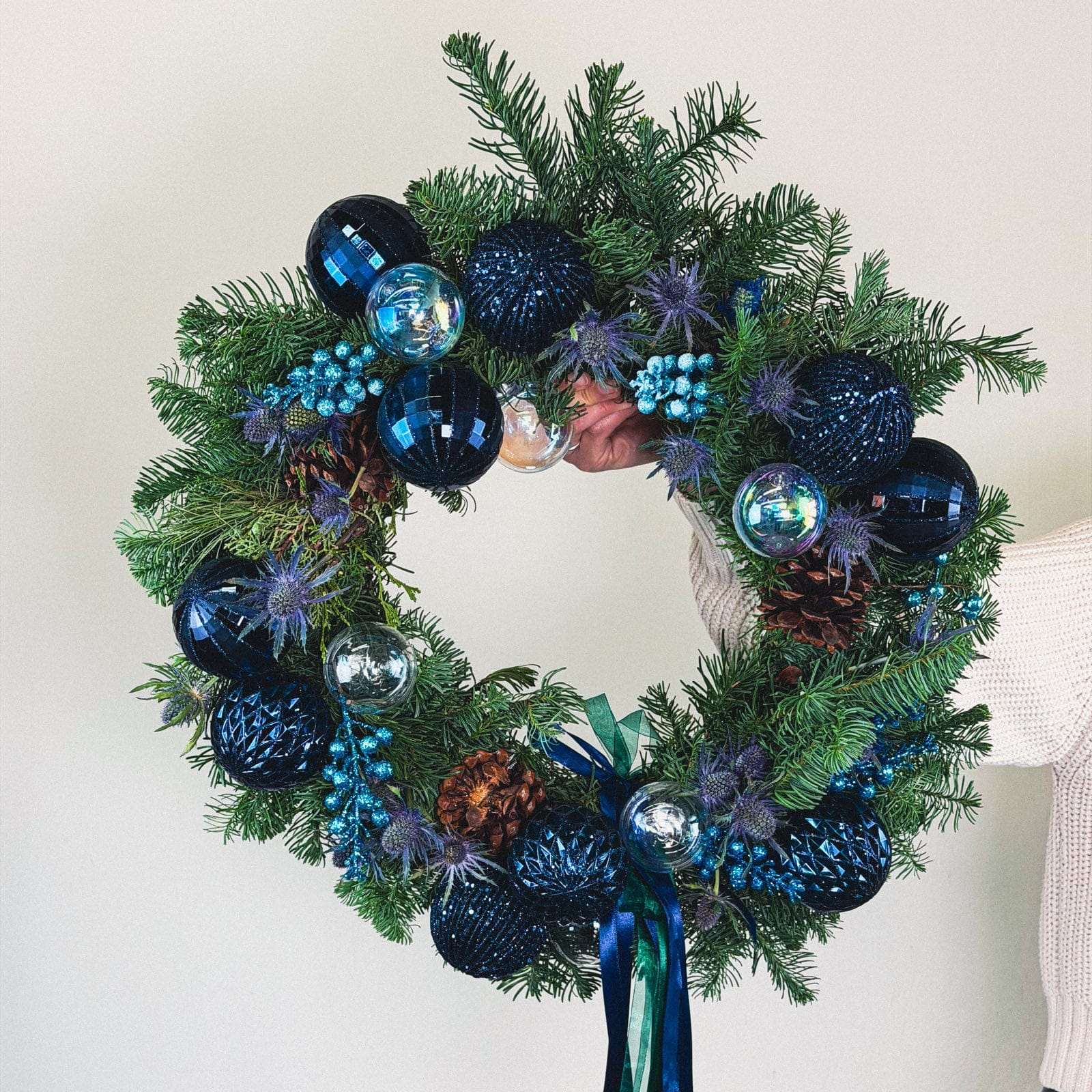 Midnight Blue Wreath with sapphire ornaments and evergreens held for display by Flowers Valley