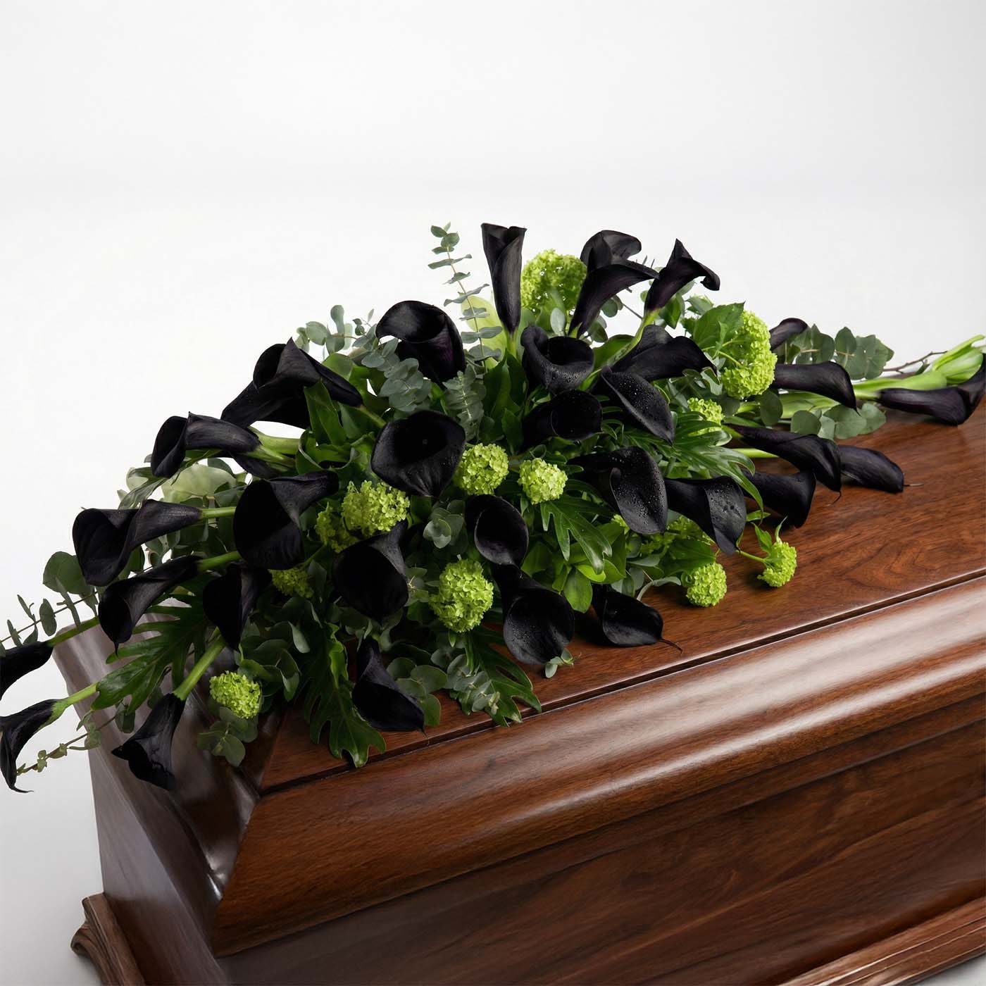 Modern casket arrangement with dark purple calla lilies and greenery