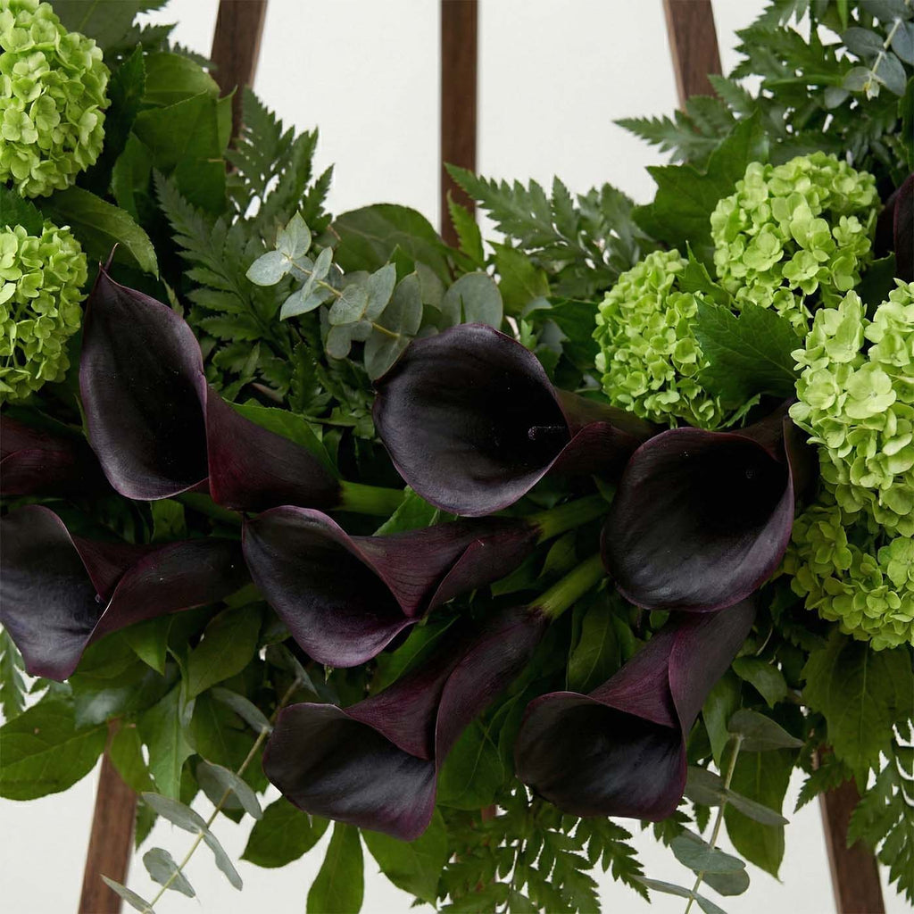 Close-up of dark purple calla lilies in modern funeral wreath