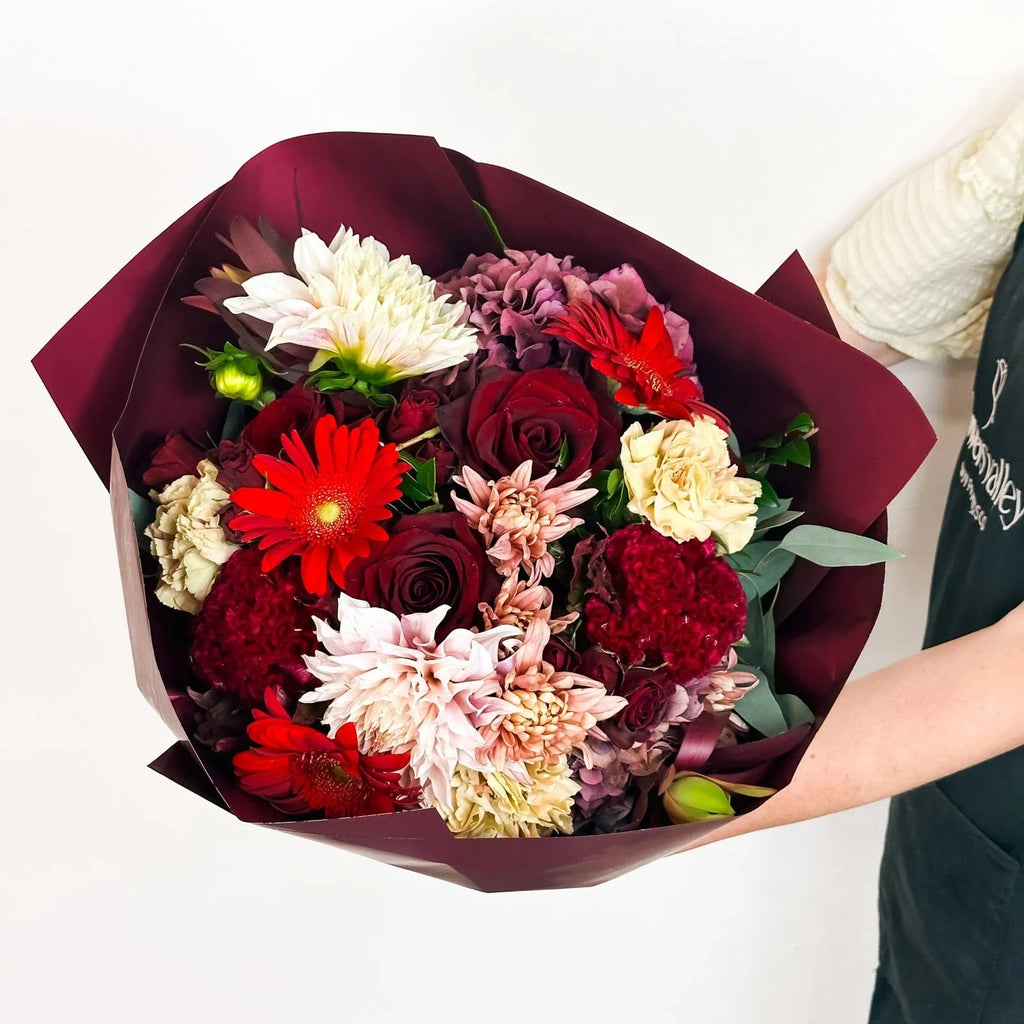 Midnight Ruby bouquet in Standard size with red roses, dahlias, and carnations wrapped in burgundy paper