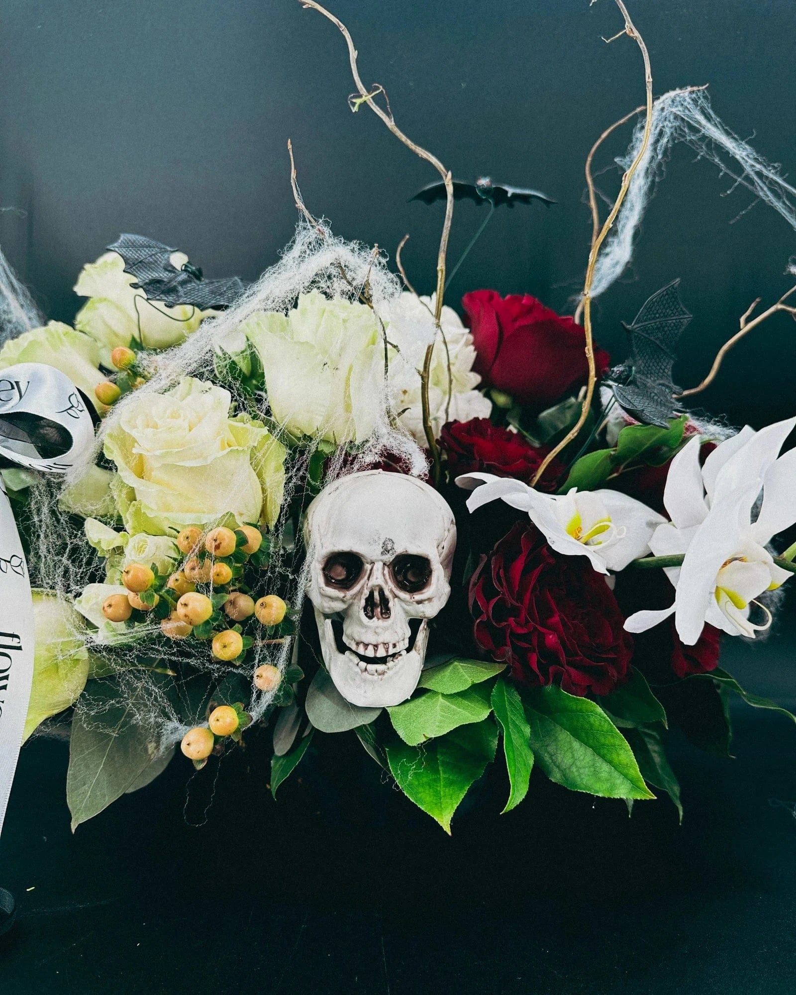 Close-up of Midnight Spell Arrangement with skull, cobwebs, ivory roses, and orchids
