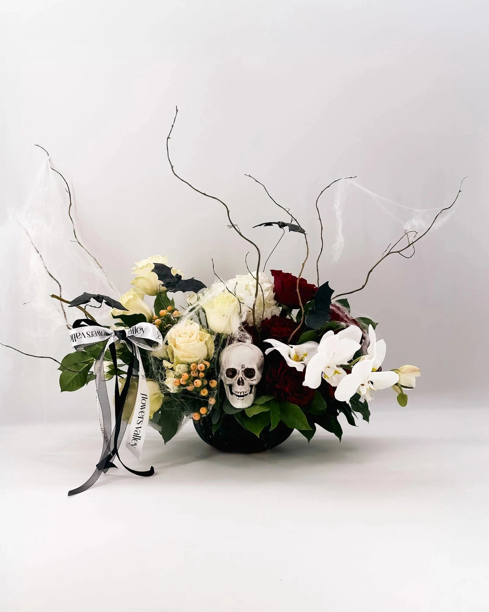 Front view of Midnight Spell Arrangement with roses, orchids, cobwebs, and bats
