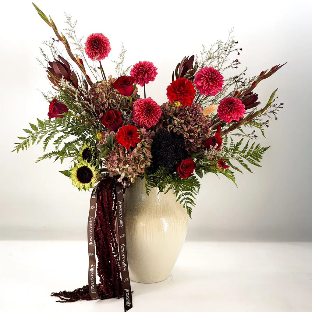 Mulberry Hearth fall flower arrangement with burgundy dahlias, red roses, antique hydrangea and hanging amaranthus in a cream ceramic vase