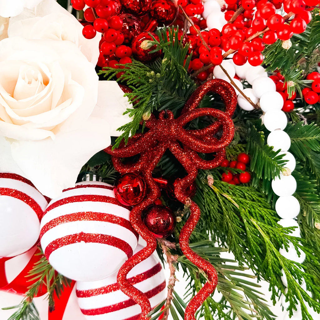 Close-up of festive red ornaments, white roses, and winter greens in Nordic-inspired holiday arrangement