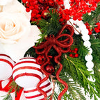 Close-up of festive red ornaments, white roses, and winter greens in Nordic-inspired holiday arrangement