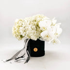 Sympathy flower arrangement with white hydrangea and cascading orchids in a black hatbox