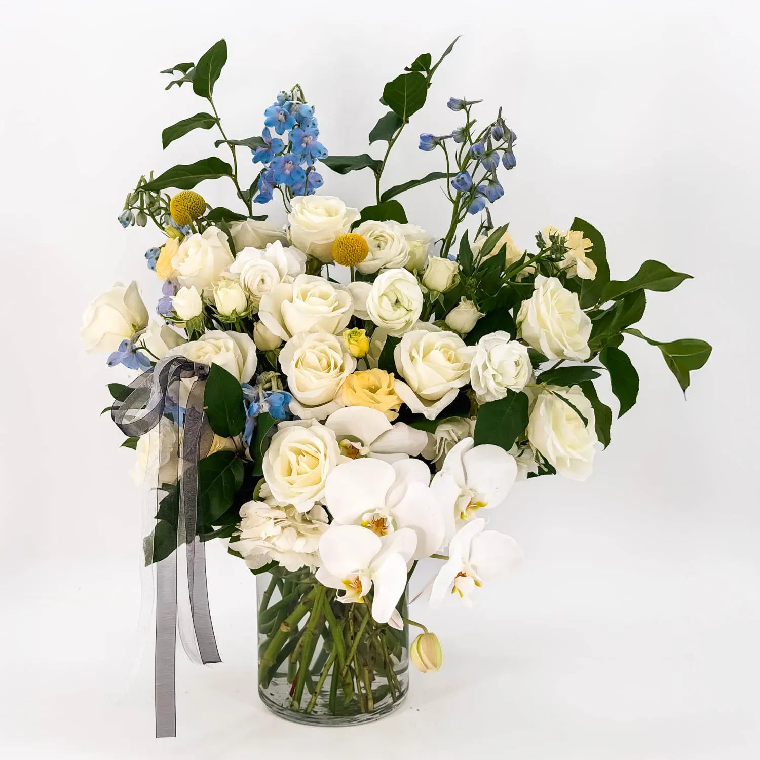 Sympathy flower arrangement with white roses, orchids, and soft blue blooms in a glass vase