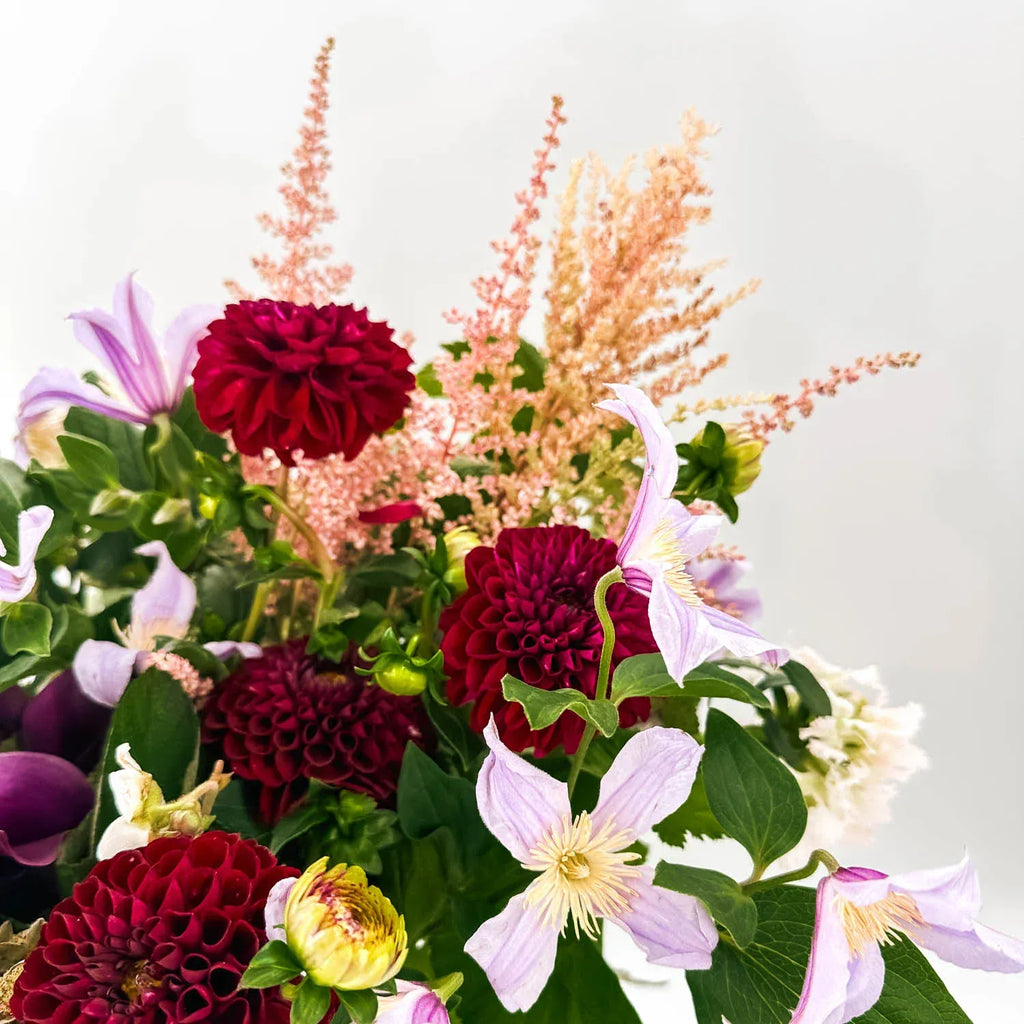 Close-up of burgundy dahlias and lavender clematis in a sympathy arrangement