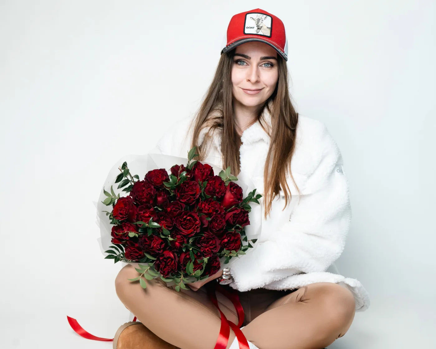 Smiling woman in a red cap holding a round bouquet of deep red roses with greenery – Flowers Valley flower delivery in Foster City, CA
