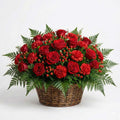 Sympathy flower basket with deep red roses, red carnations, hypericum berries, and evergreen fern greenery arranged in a full floral design.