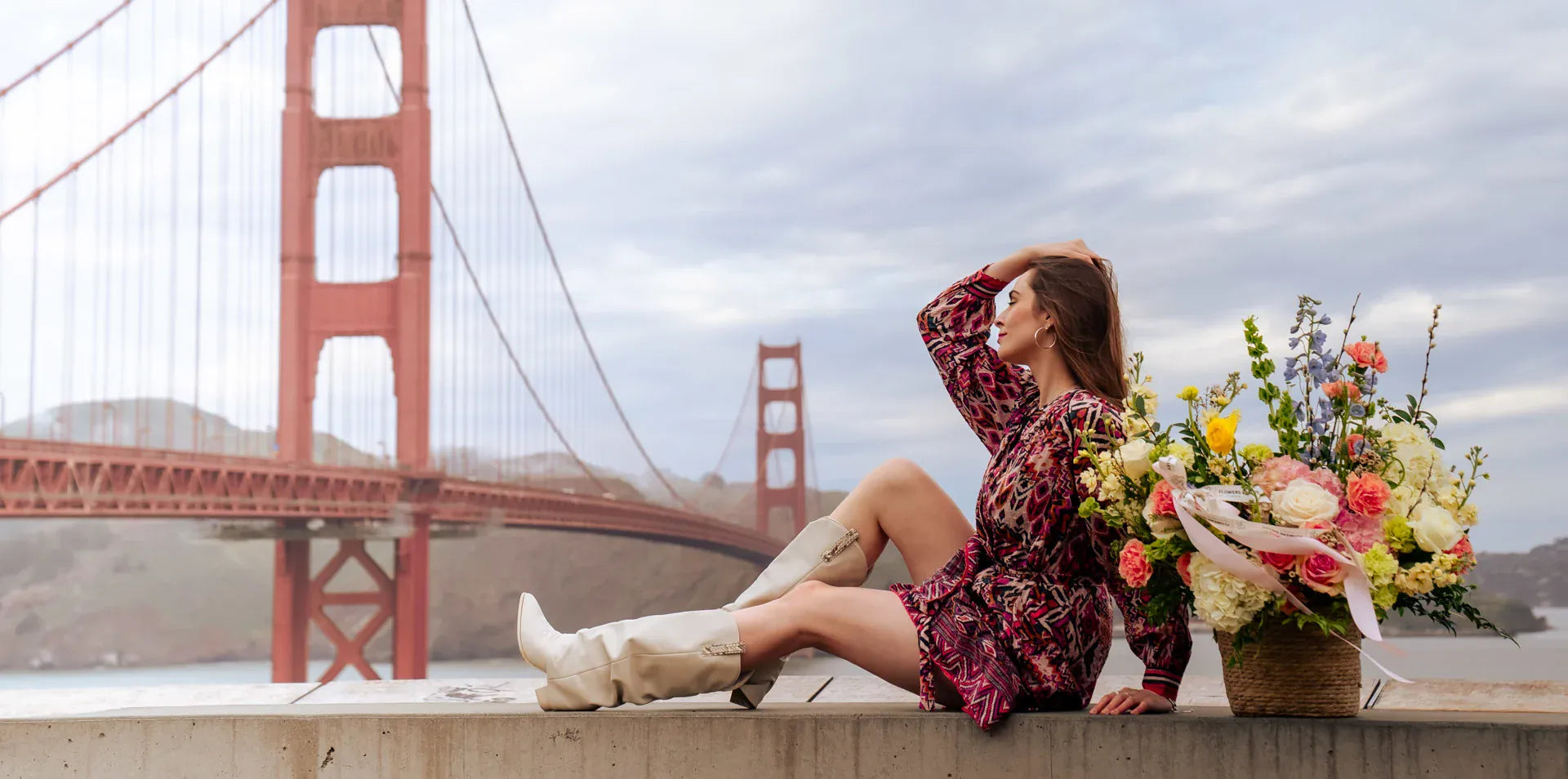 Woman sitting on a ledge with a bouquet of flowers in front of the Golden Gate Bridge.