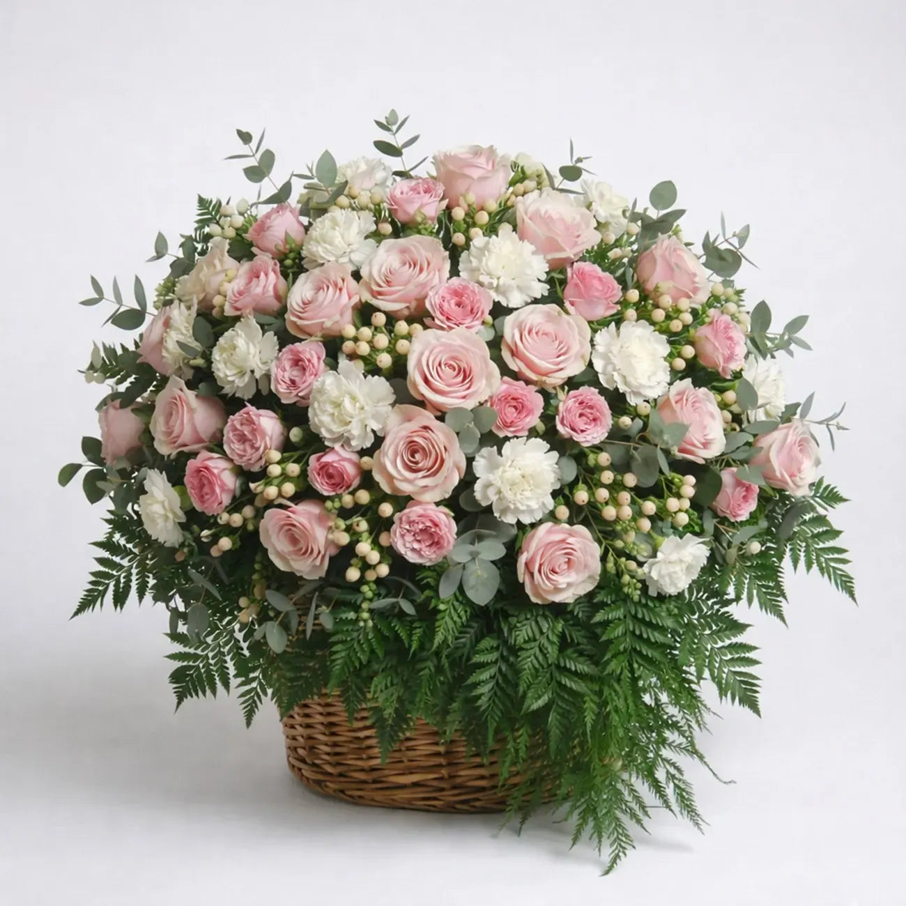 Sympathy flower basket with blush roses, white carnations, eucalyptus, and fern greenery arranged in a dense floral design.
