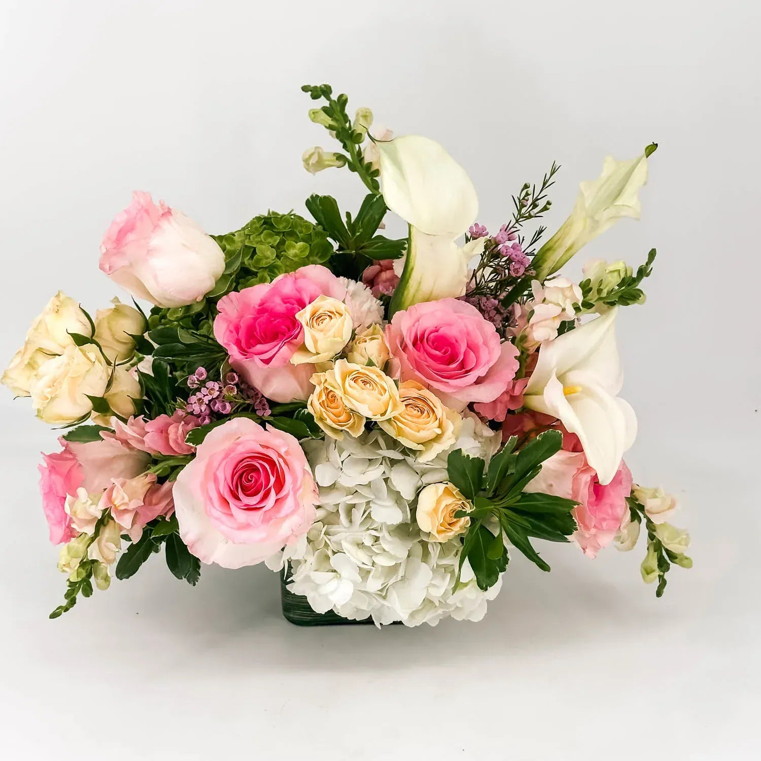 Close-up of pink roses, calla lilies, and white hydrangea in a sympathy arrangement