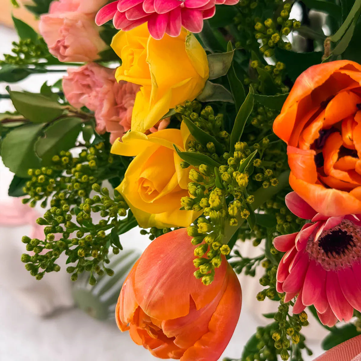 Close-up of pink gerbera daisies, orange tulips, and yellow craspedia in spring vase arrangement