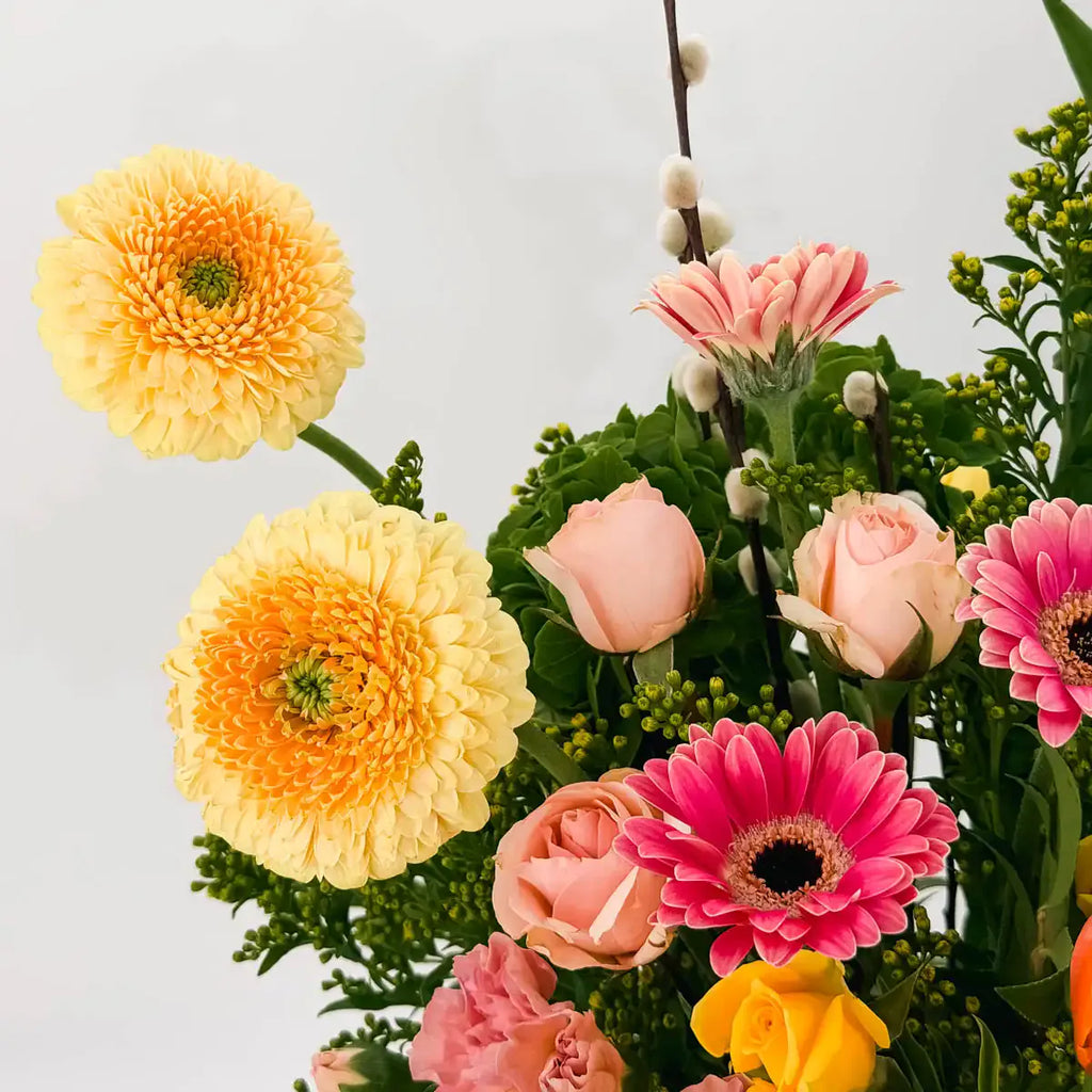 Close-up of yellow pon-pon ranunculus, pink gerbera daisies, and peach spray roses in the Sunlit Garden arrangement — Flowers Valley