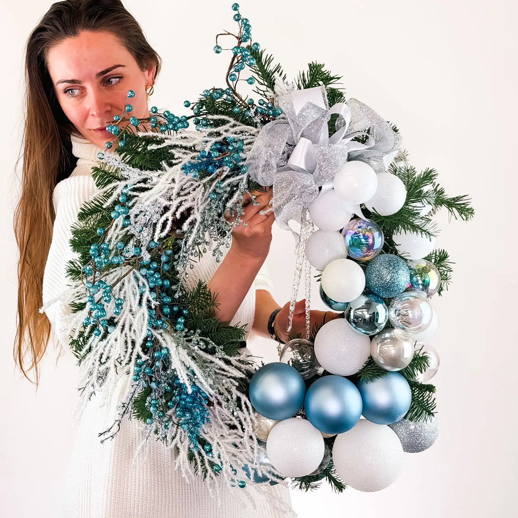 Handcrafted winter wreath with icy blue and white ornaments held by woman in white sweater.