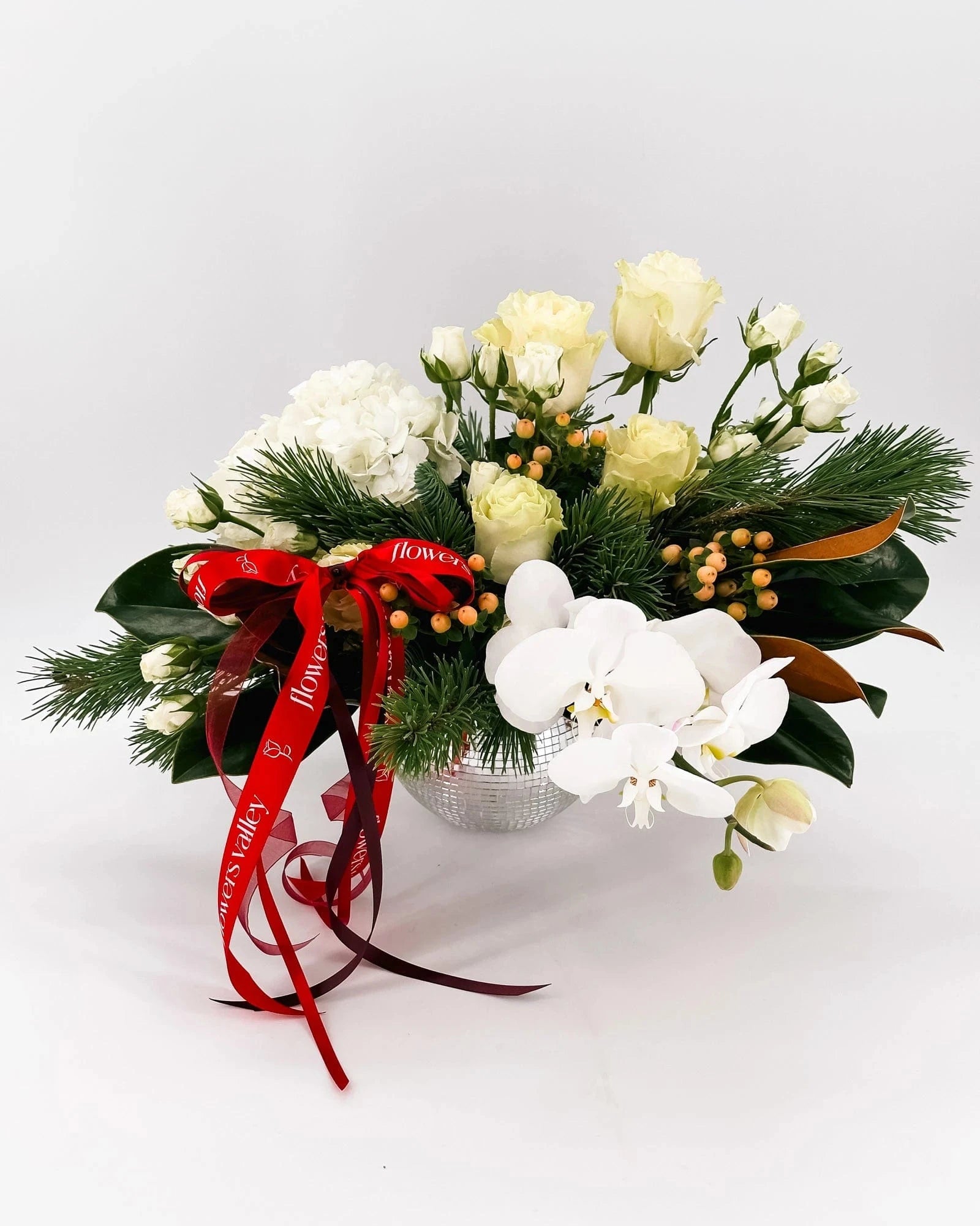 Winter Grace Arrangement with white roses, hydrangeas, orchids, berries, and holiday greenery in silver vase