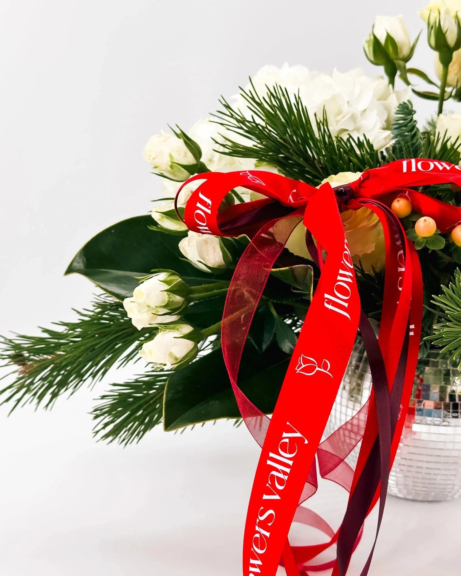 Close-up of Winter Grace Arrangement with red ribbon, white roses, and evergreen accents