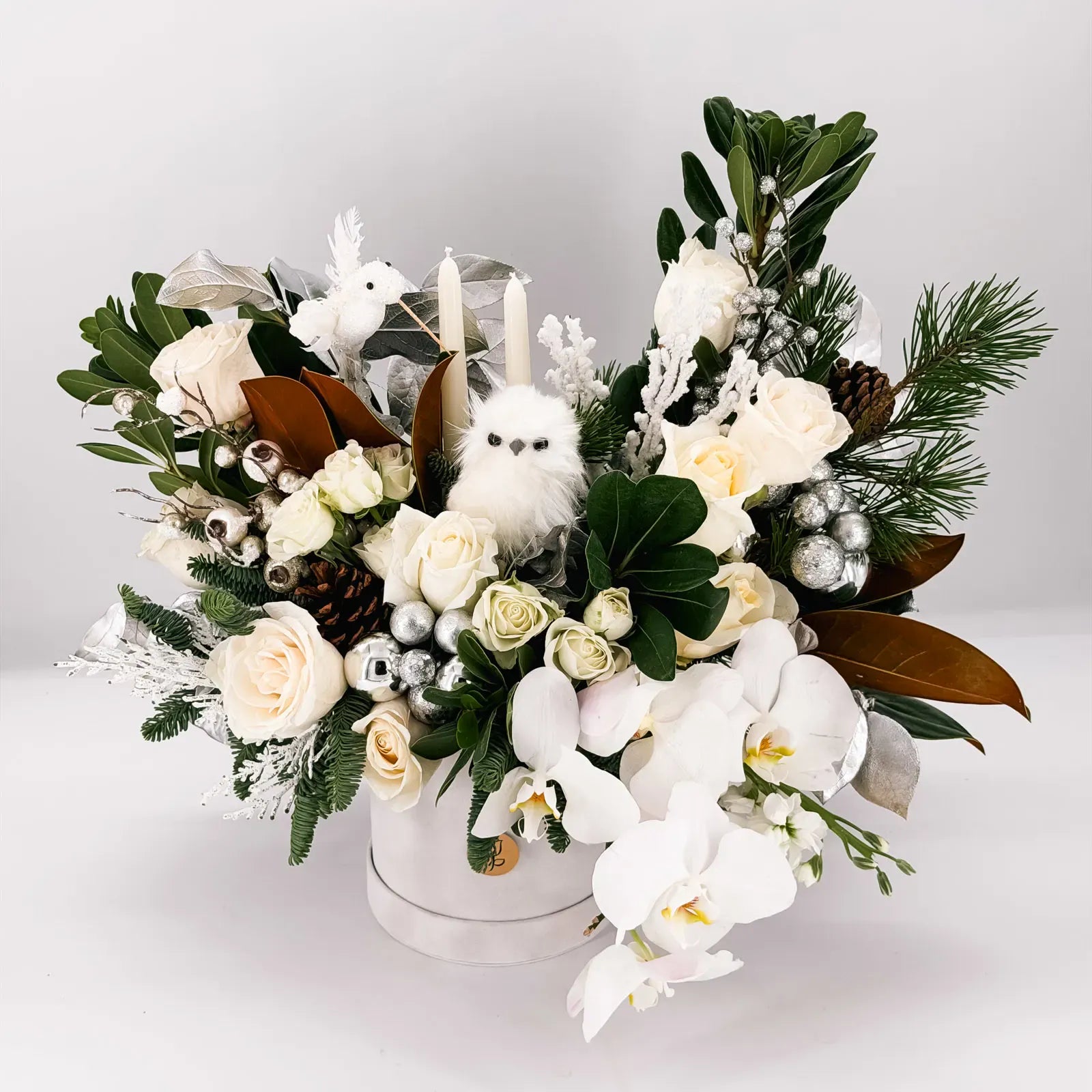 Elegant winter floral arrangement with orchids, roses, greenery, and silver decor