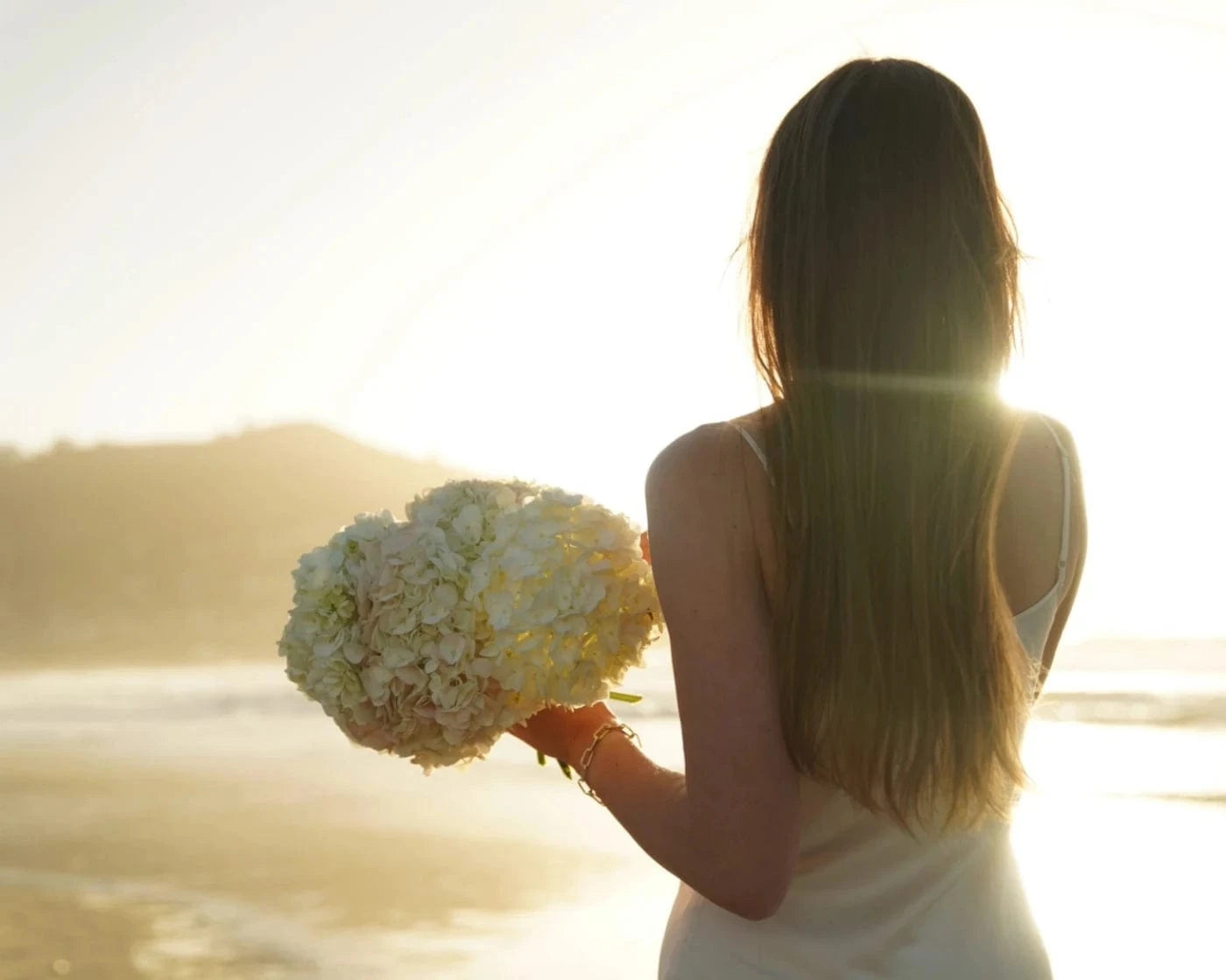 Woman holding a bouquet of white hydrangeas at the seaside, back view in soft sunlight – Flowers Valley Half Moon Bay flower delivery